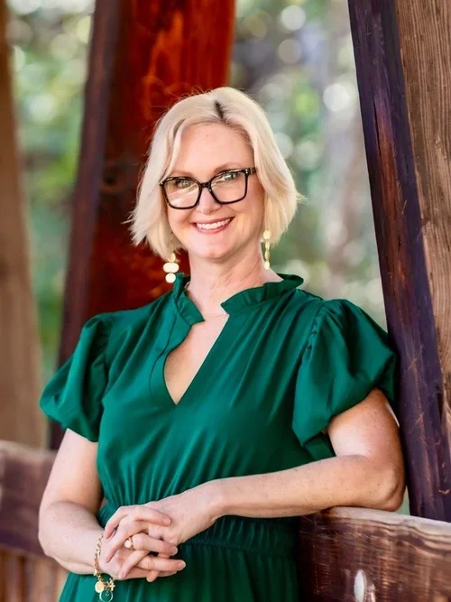 Kara Pepper, MD, smiling wearing a dark green dress and leaning on a wooden railing