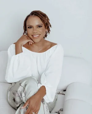 Miranda Campbell, Licensed Clinical Social Worker, smiling wearing a white long-sleeved off-the-shoulder top and resting her hand under her chin