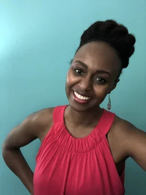 Dr. Monica Blied, Licensed Clinical Psychologist, Brainspotting therapist, and Health Coach, smiling wearing a vibrant pink tank top against a teal wall