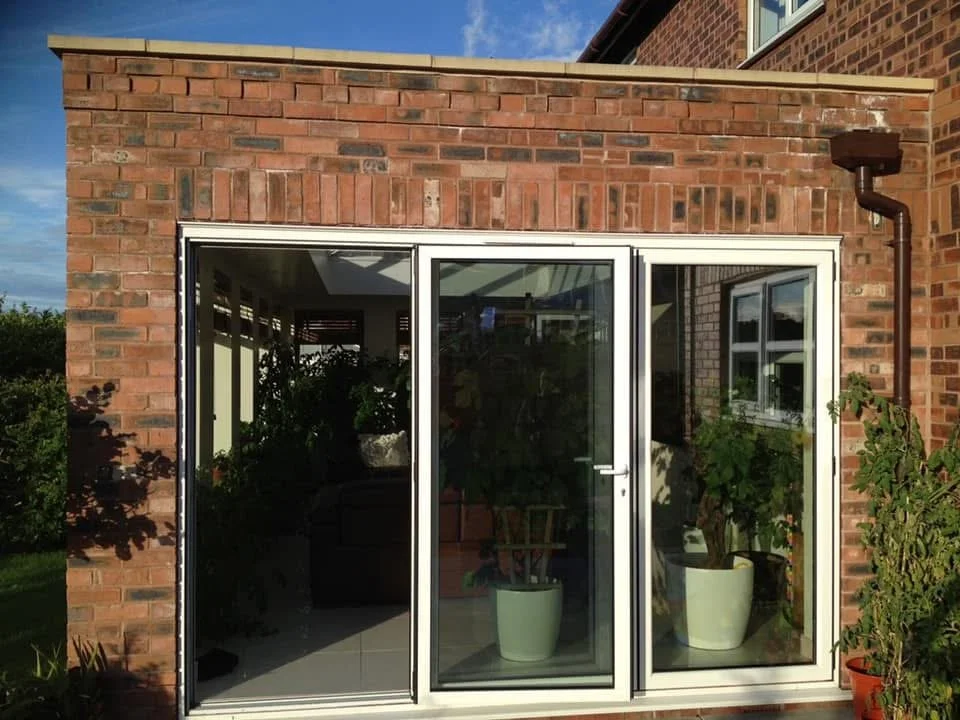A brick house with a sliding glass door leading to a garden or patio area, with plants inside and outside.