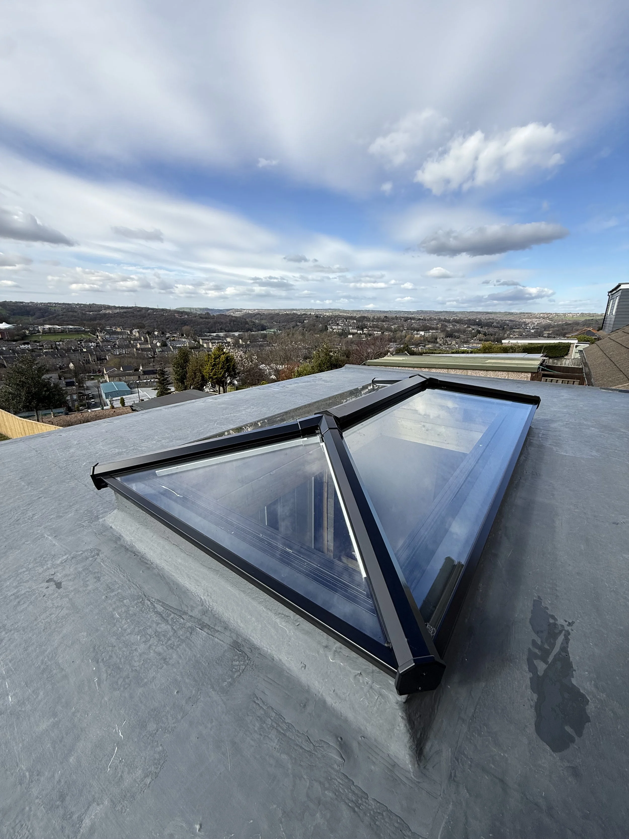 A triangular skylight on a flat rooftop, with a scenic cityscape and cloudy sky in the background.