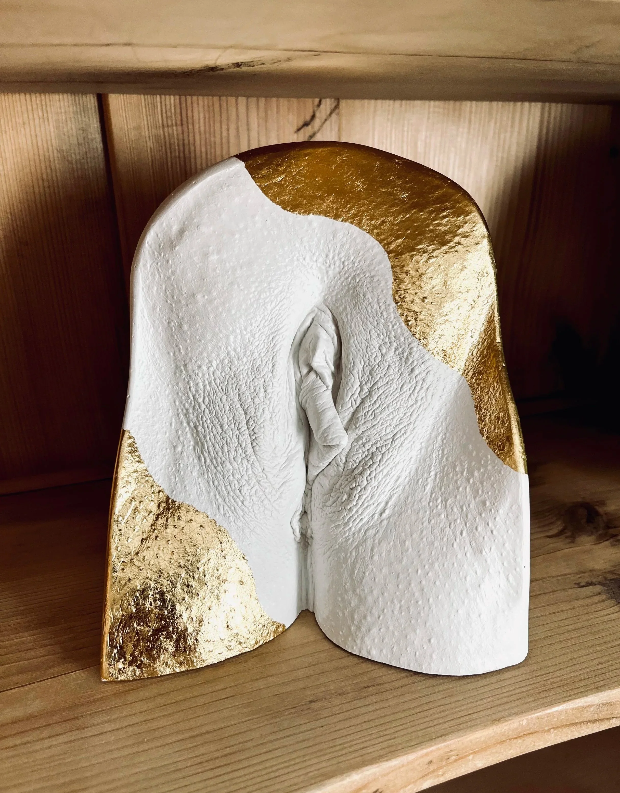 Vulva-Cast aus Gips mit goldfarbener Blattmetall-Veredelung.