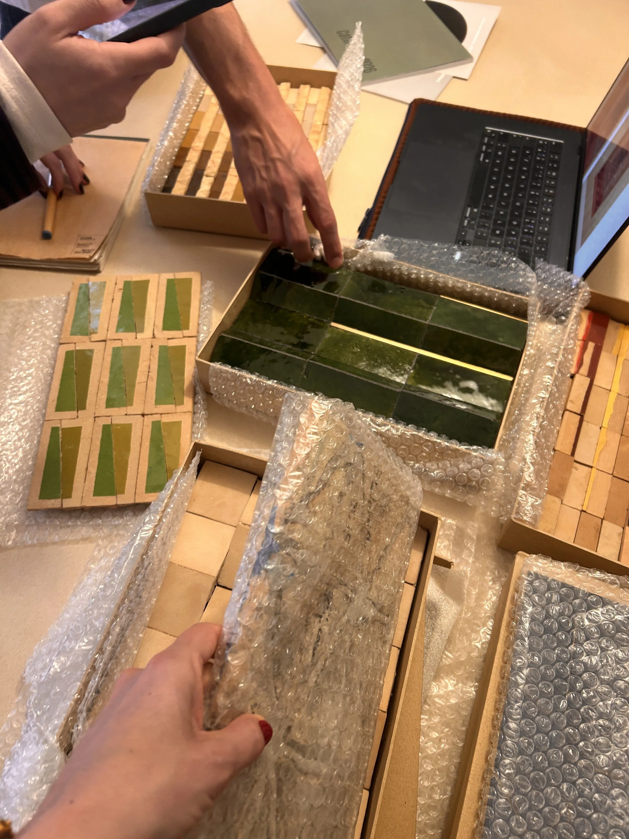 Personne manipulant des échantillons de carrelage ou de matériau de construction, entourée de bulles de plastique à bubules, avec plusieurs livres ouverts et une boîte remplie de carreaux