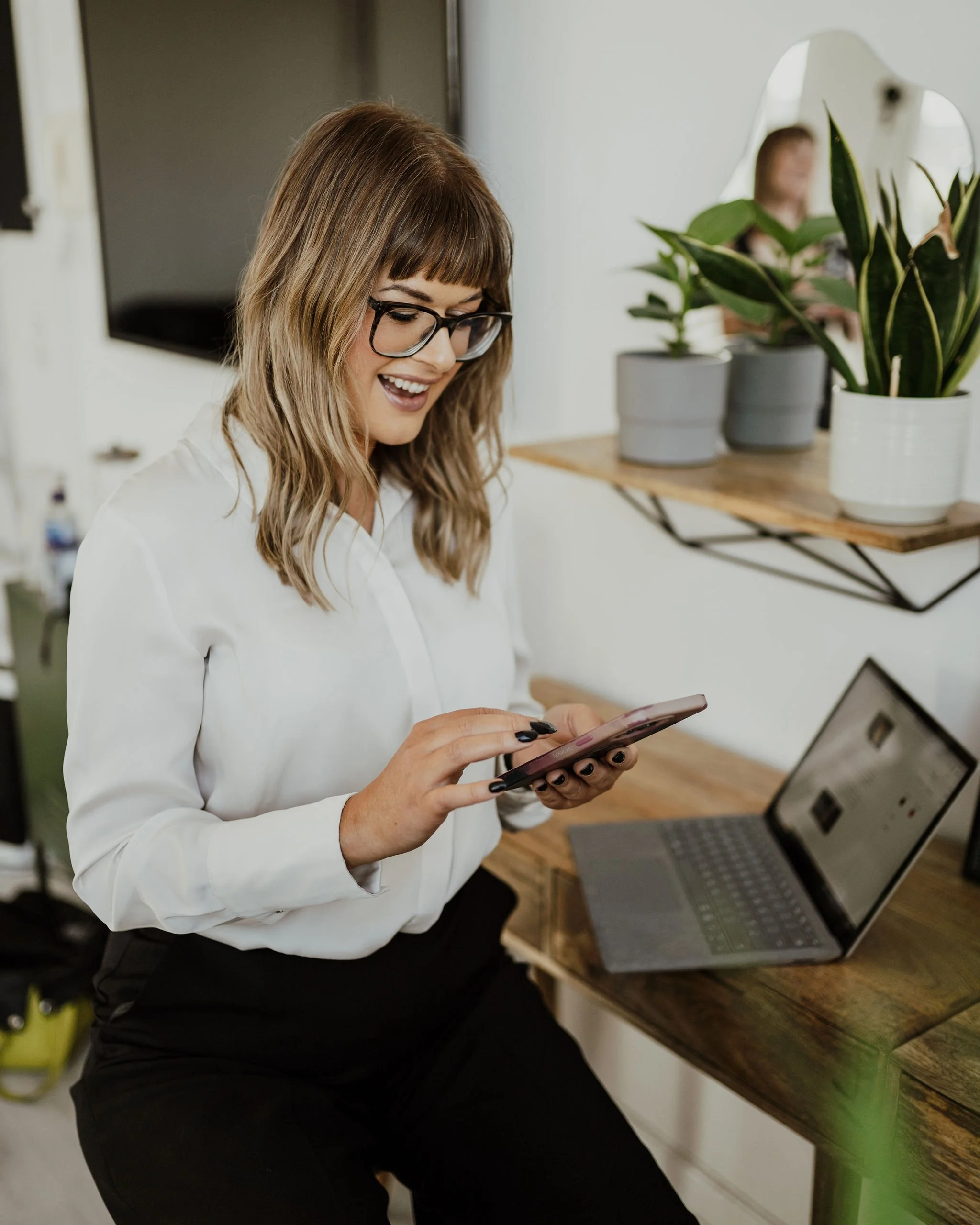 Sarah Stewart sitting at a desk with her laptop and tapping into her mobile phone