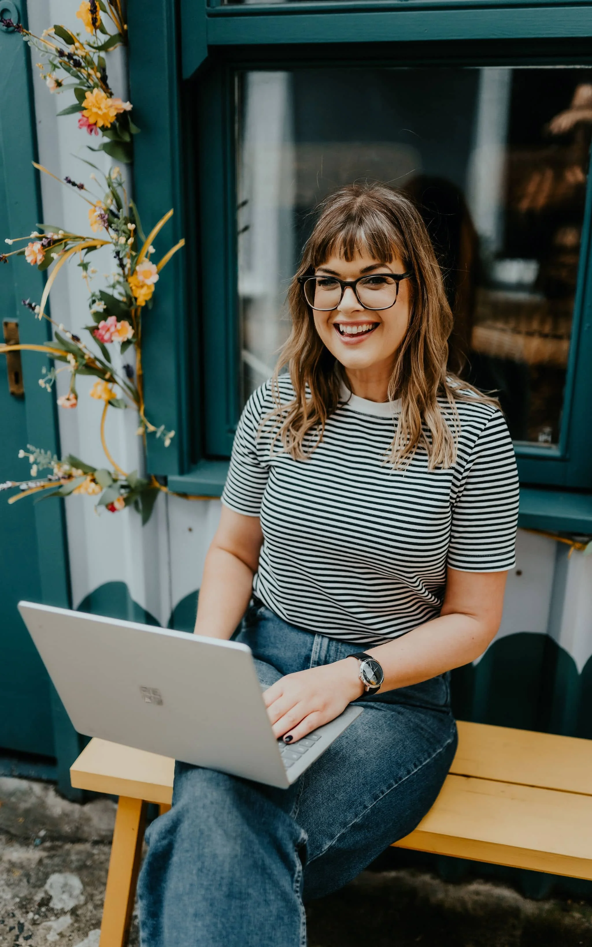 sarah stewart smiling whilst sitting on a bench with her laptop