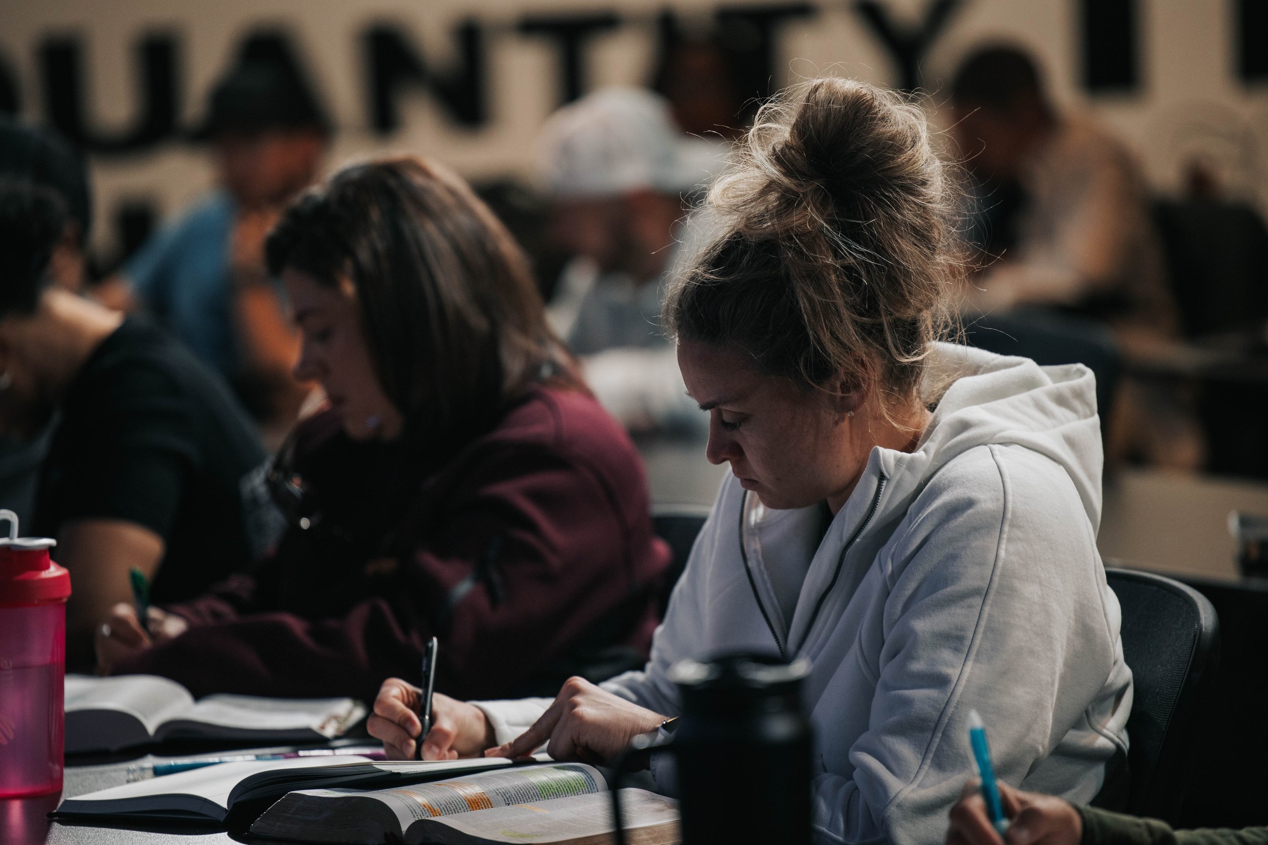 A group of students taking notes or studying at a classroom or library setting, with books open in front of them and focusing on their work.