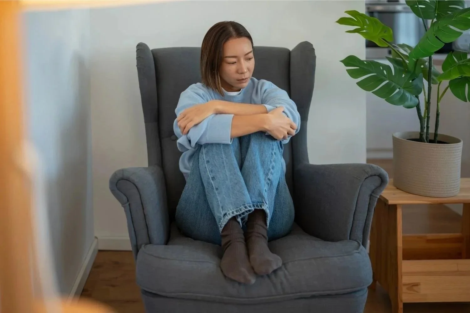Woman sitting alone in a chair appearing overwhelmed and anxious, from OCD, intrusive thoughts, and anxiety. 