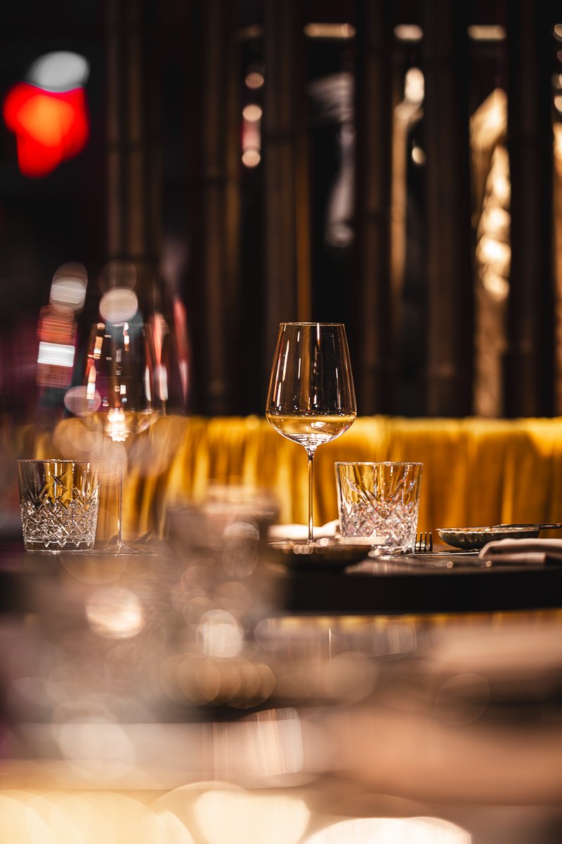 Ein leeres Weinglas auf einem Restauranttisch mit zwei Kristallgläsern, einem dunklen Hintergrund und gedämpfter, warmer Beleuchtung.