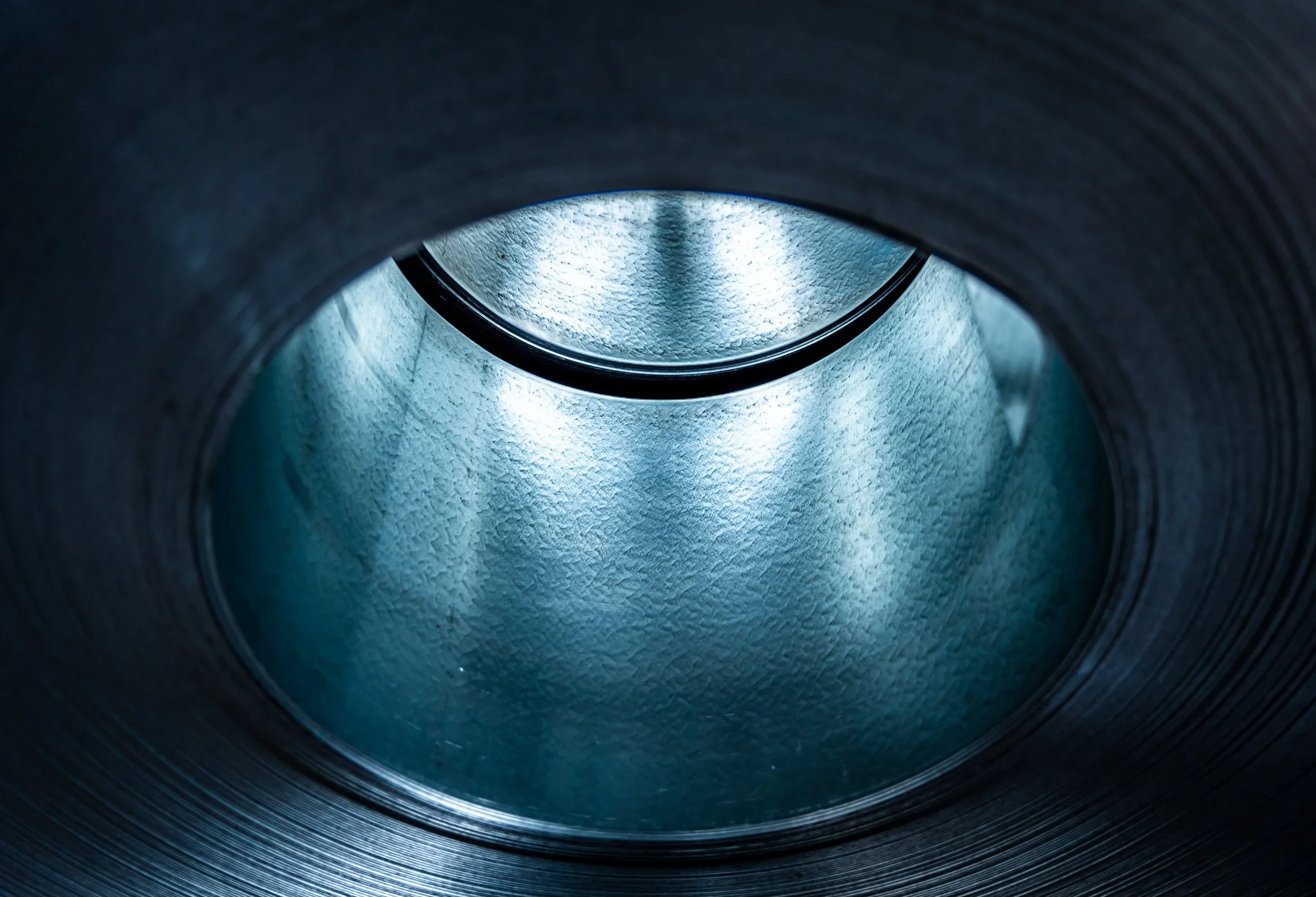 Nahaufnahme eines industriellen Metallrohrs oder -zylinders mit strukturierter Innenfläche, beleuchtet von kühlem blauem Licht.