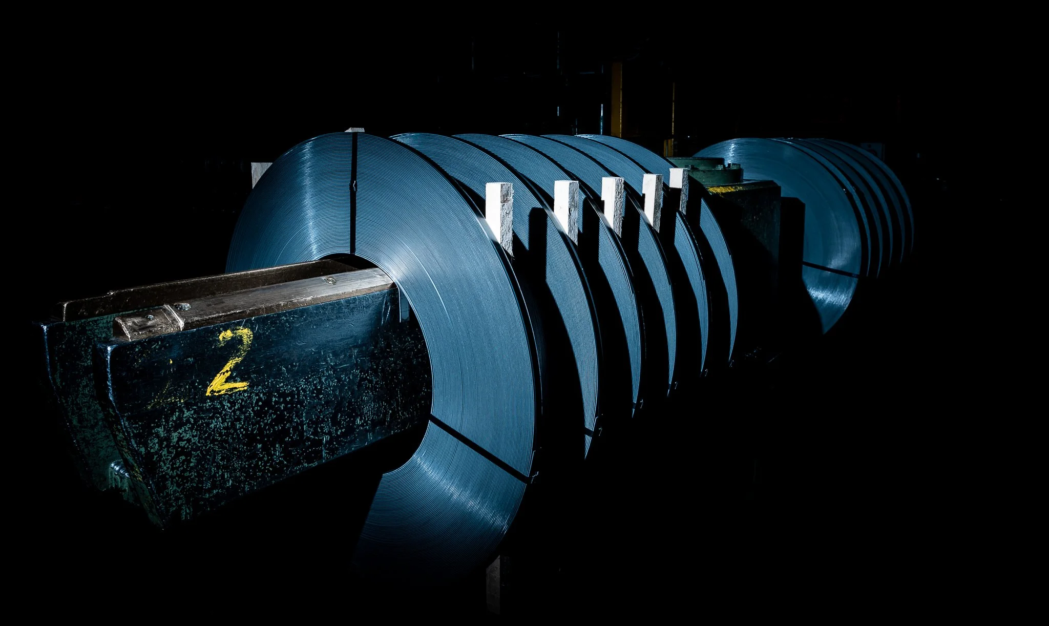 Große Metallspulen, die in einer dunklen Industriehalle gelagert sind.