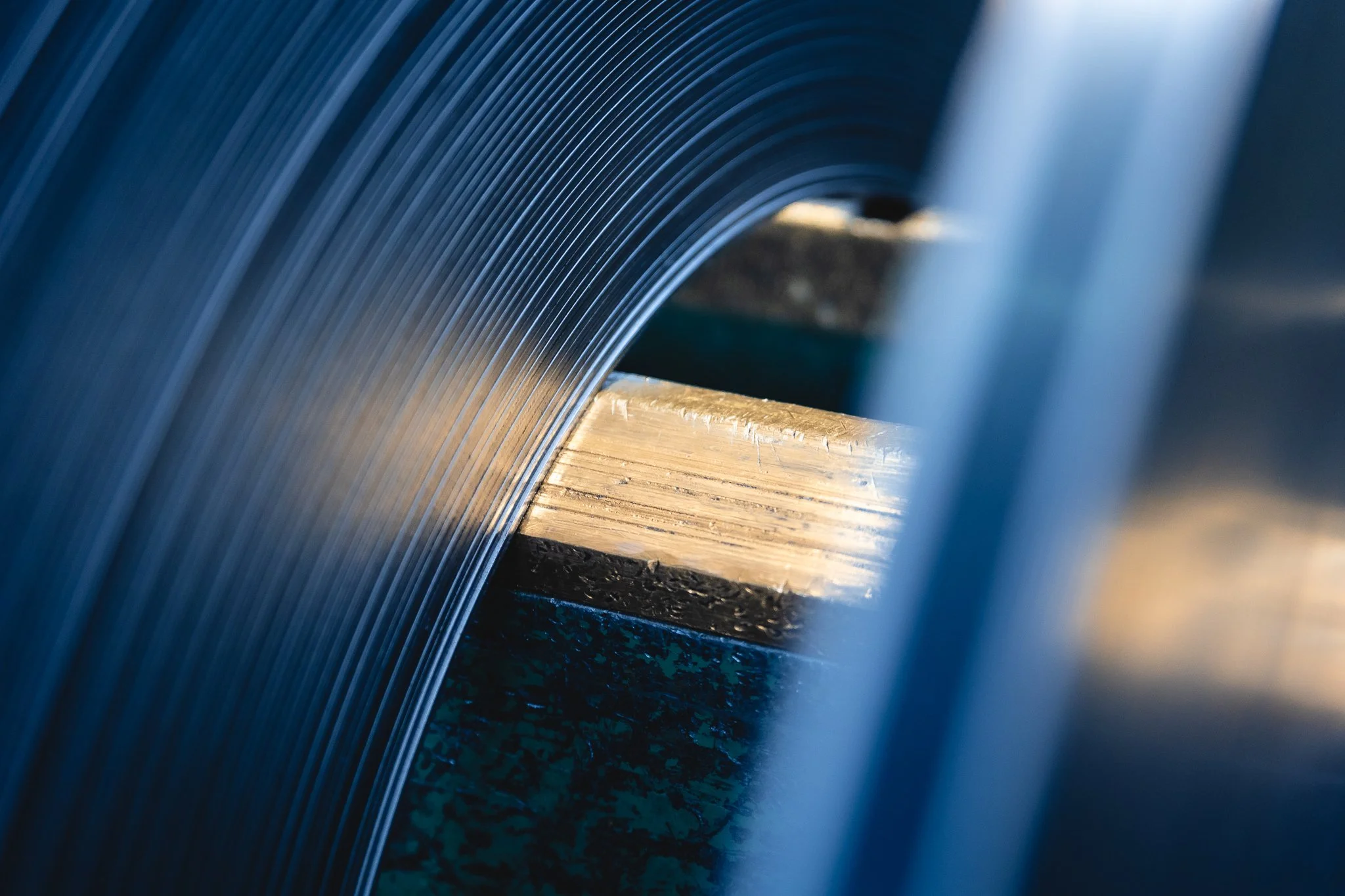 Nahaufnahme einer Metallspule, die auf einer strukturierten Oberfläche aus Holz und Beton liegt, wobei der Fokus auf den glänzenden, geschwungenen Metallkanten liegt.