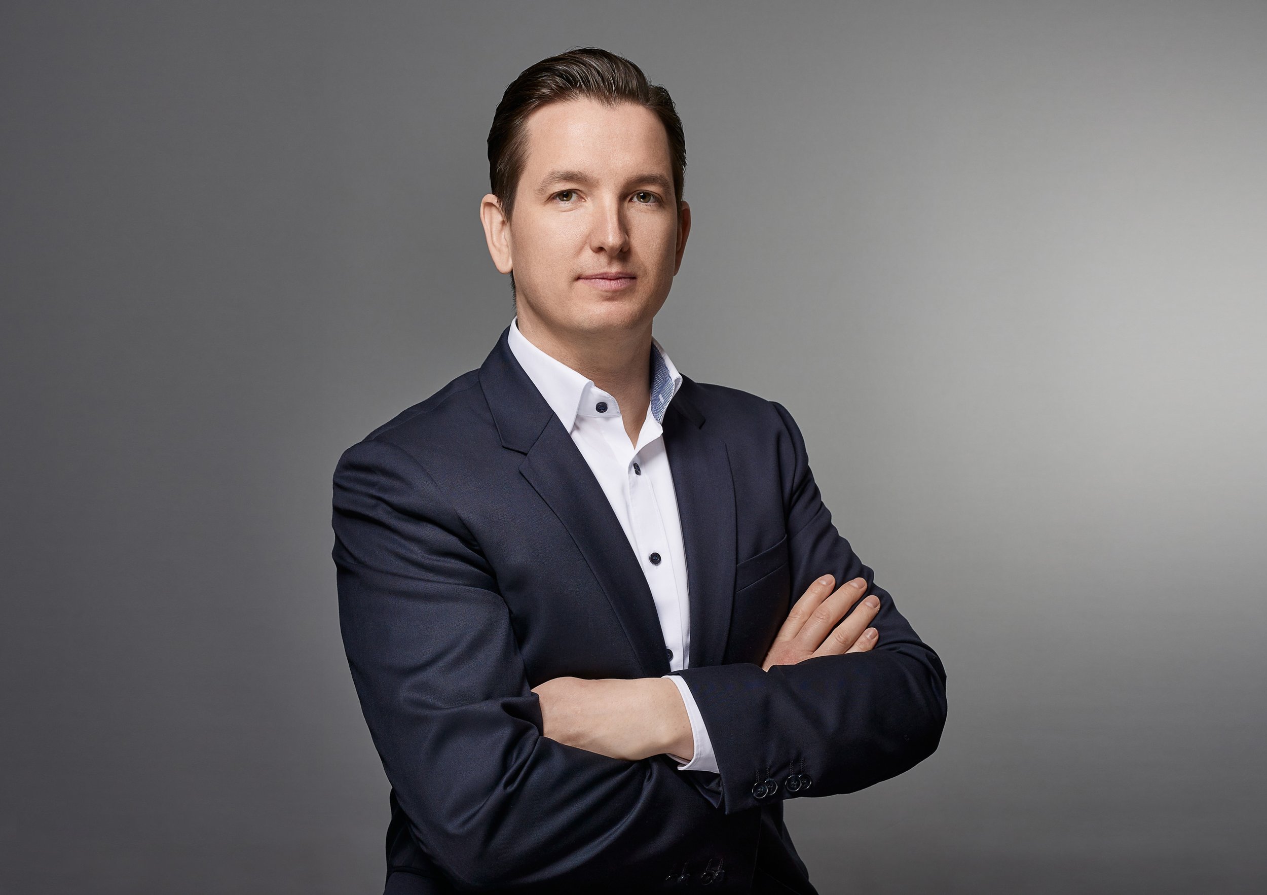 Business Porträt eines Mannes in formeller Kleidung mit ausgestrecktem Arm vor grauem Hintergrund.