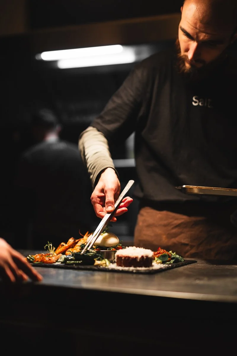 Ein Koch mit Bart, der in einer Küche oder einem Restaurant ein Gericht auf einem Teller anrichtet