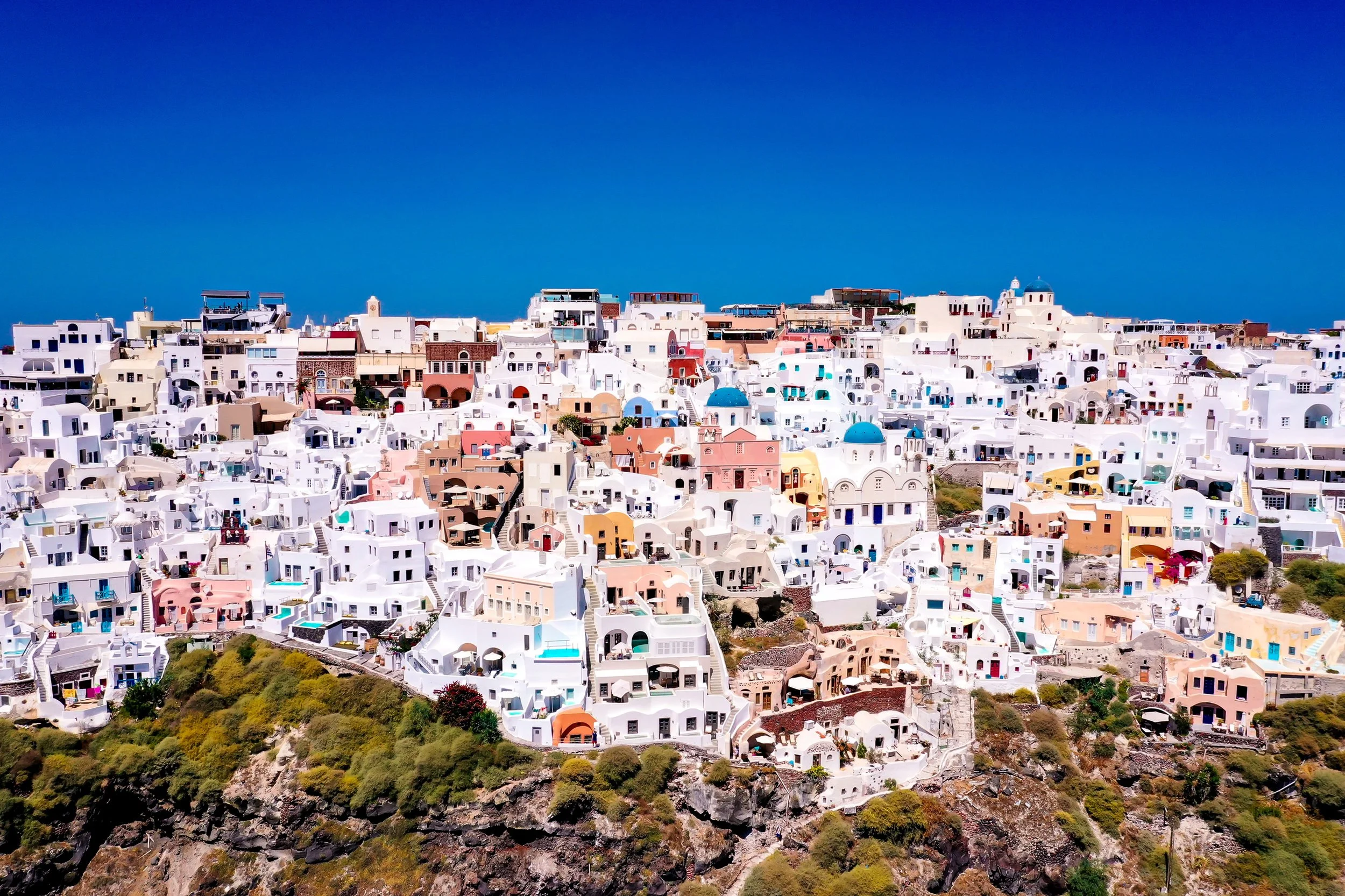 Bunte weiße Häuser an steiler Hanglage auf der Insel Santorini mit blauem Himmel im Hintergrund.