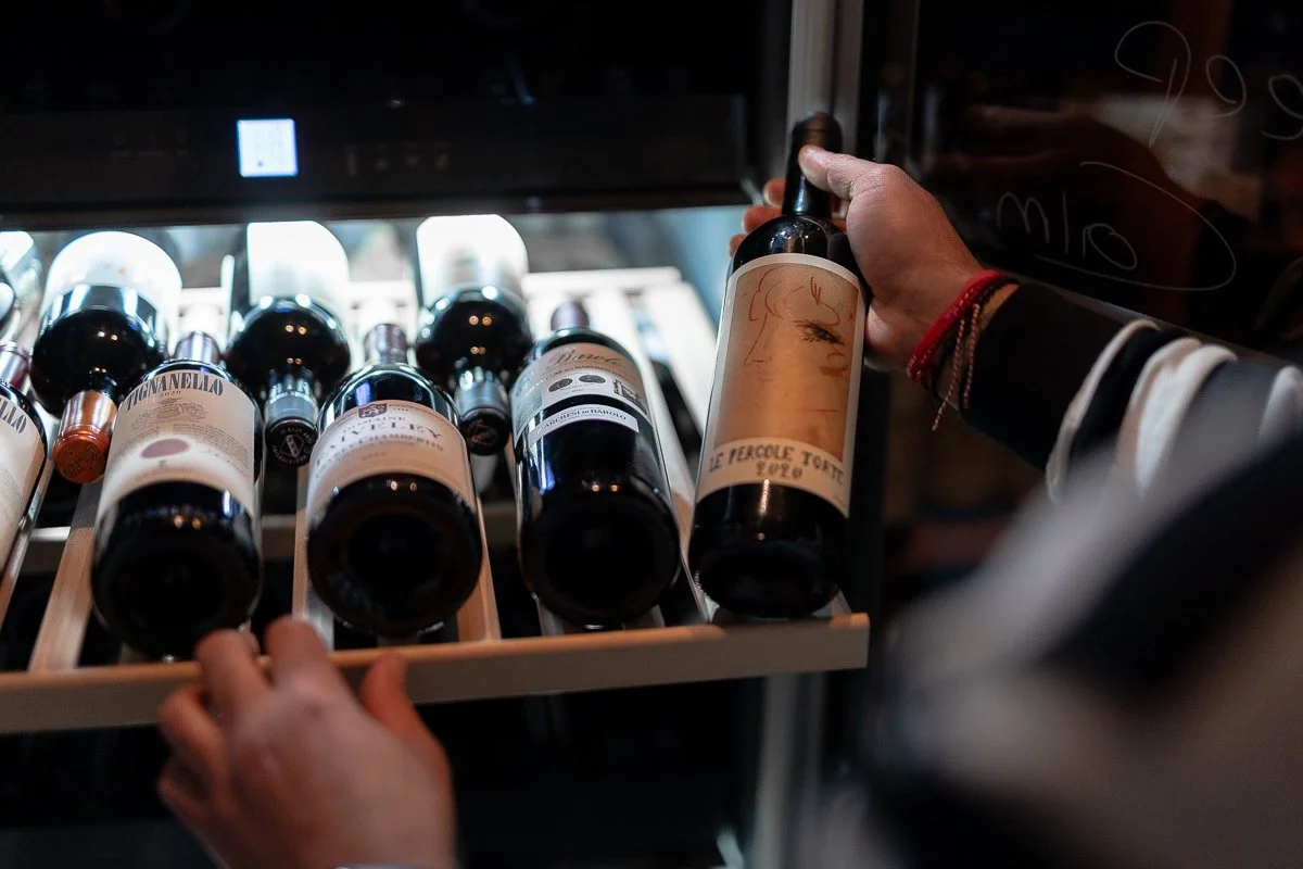 Eine Hand greift eine Flasche Wein aus einem Weinkühlschrank, neben anderen Weinflaschen.