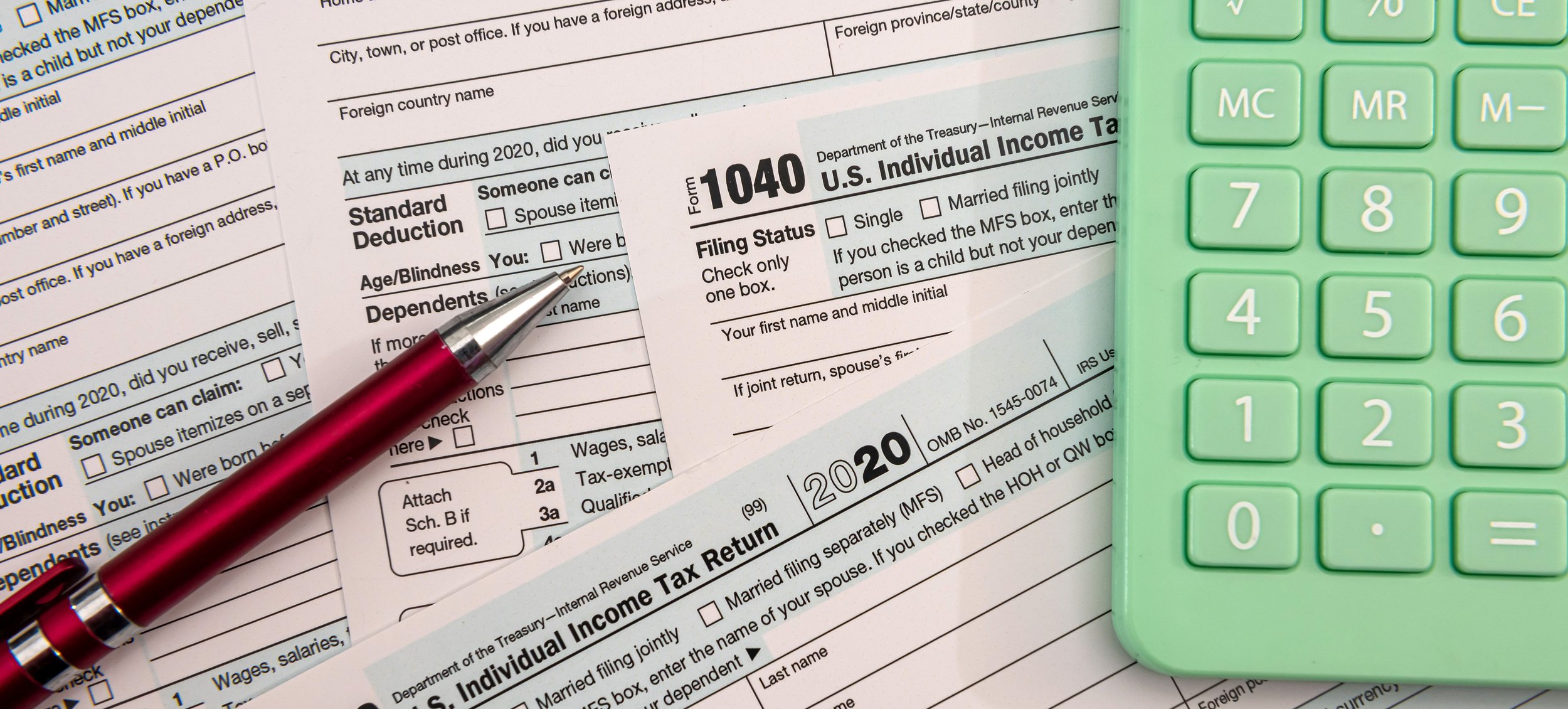 U.S. tax forms, a red pen, and a green calculator on a desk.