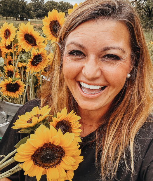 A woman smiling outdoors surrounded by sunflowers at The Flower Meadow You Pick Flower Farm and Barnyard Petting in Coweta, Ok