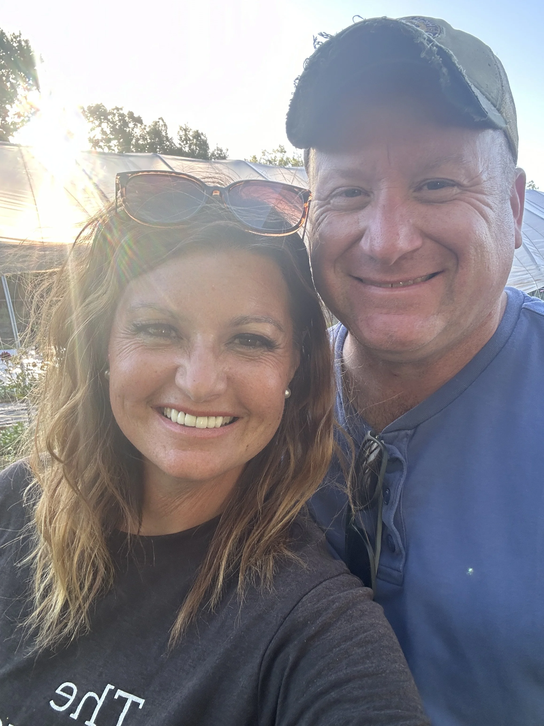 A smiling woman and a smiling man taking a selfie outdoors in natural sunlight, at The Flower Meadow You Pick Flower Farm and Barnyard Petting in Coweta, Ok