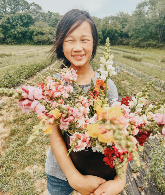 Girl smiling and holding a bouquet of colorful flowers in a garden.