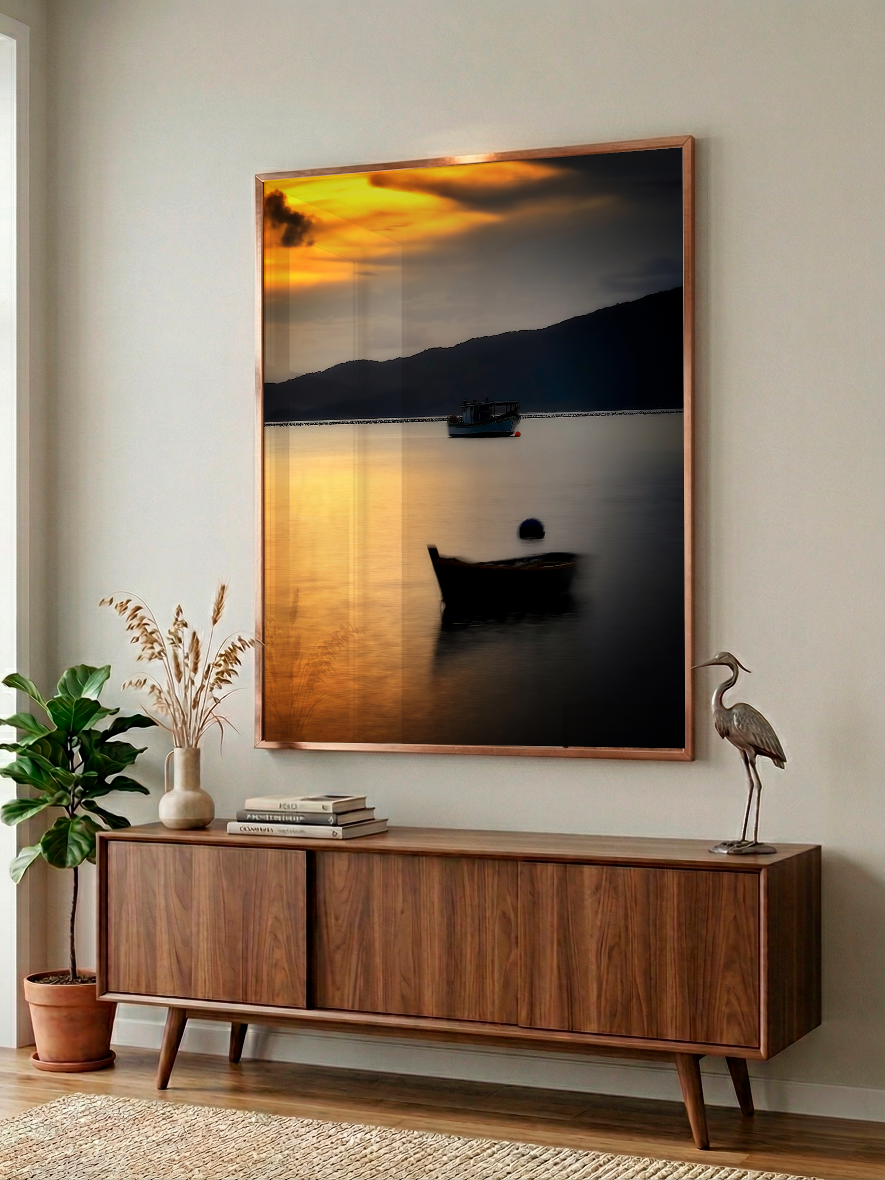 Quadro de pôr do sol imerso em uma parede branca, acima de um móvel de madeira, com uma planta, livros e uma escultura de uma garça na decoração.