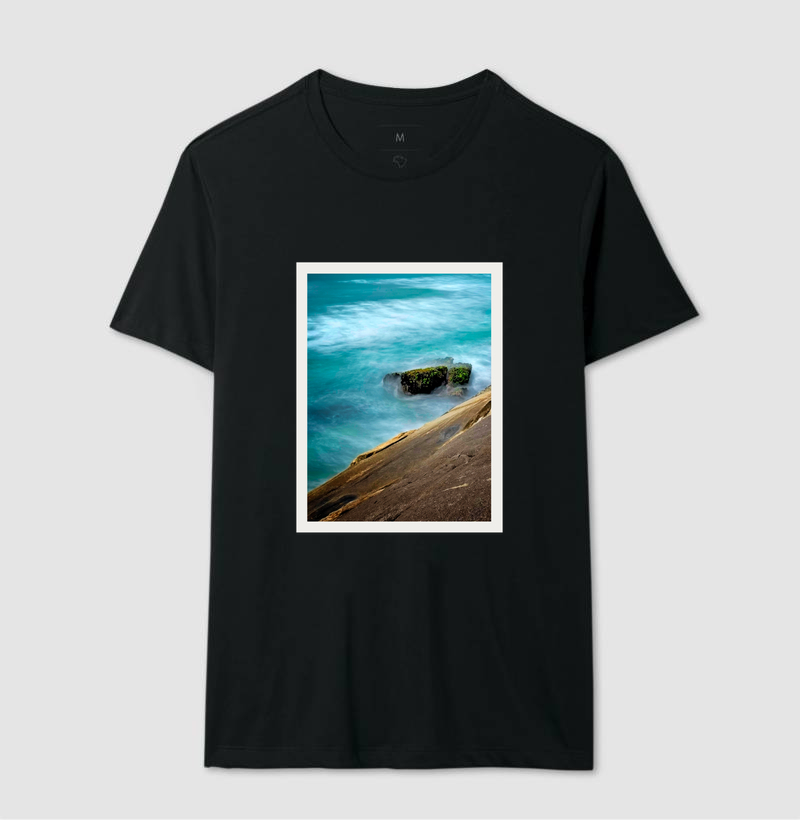 Camiseta preta com estampa de uma paisagem marítima, com água azul, rochas e um trecho de uma encosta.