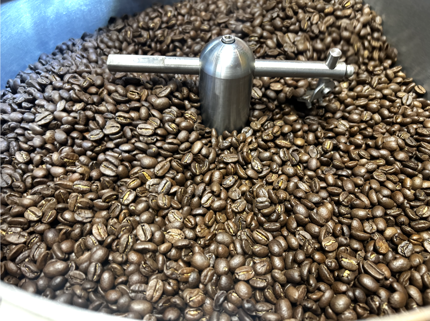 Close-up of roasted coffee beans being processed in a metal container with a mechanical arm.