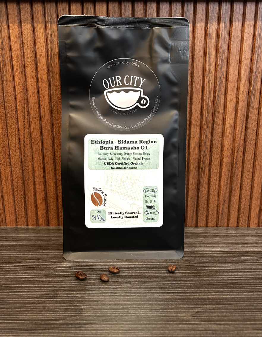 Package of Ethiopian coffee from the Sidama region with label showing details, placed on a wooden surface with four coffee beans in front.