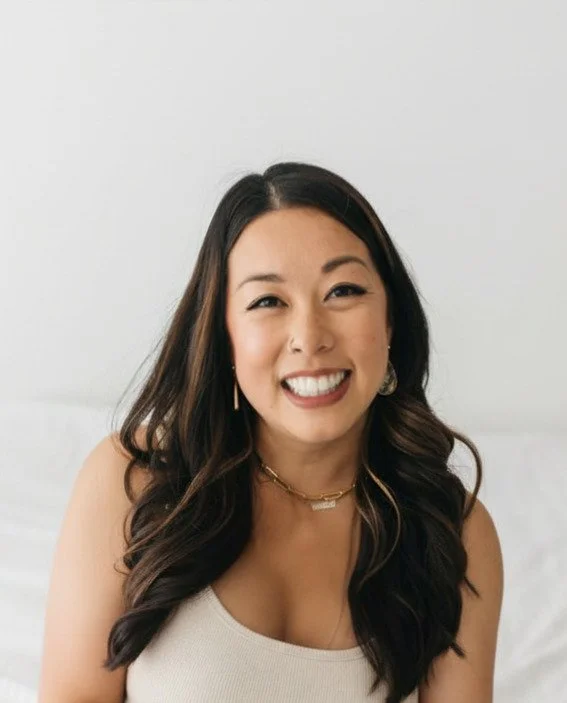 Portrait of Jess, owner of Jess Toda, SLP smiling with long dark hair, wearing a beige top and gold jewelry, sitting against a plain white background.