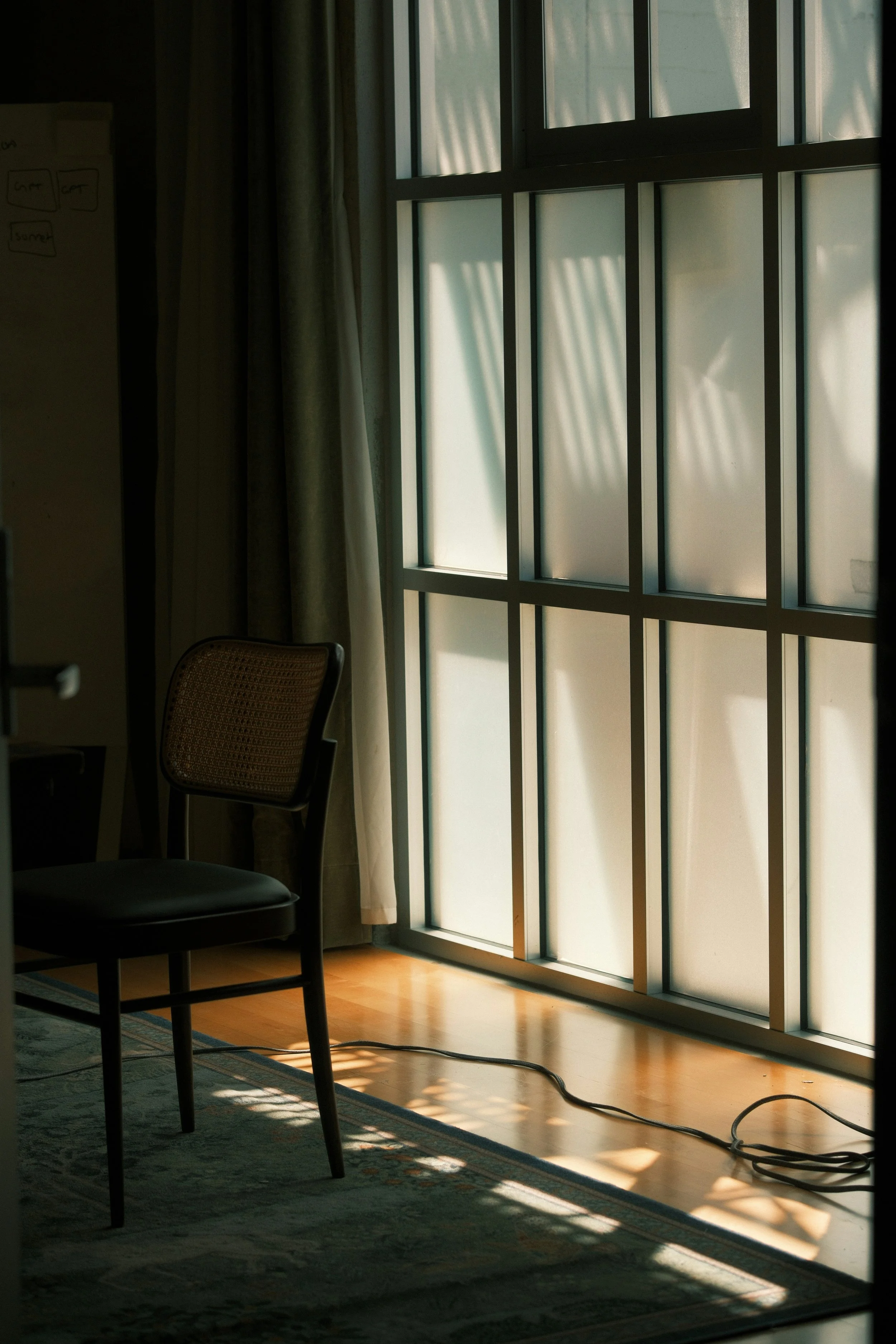 Une pièce avec une grande fenêtre qui laisse entrer la lumière, un fauteuil, un tapis sur le sol et un câble électrique.