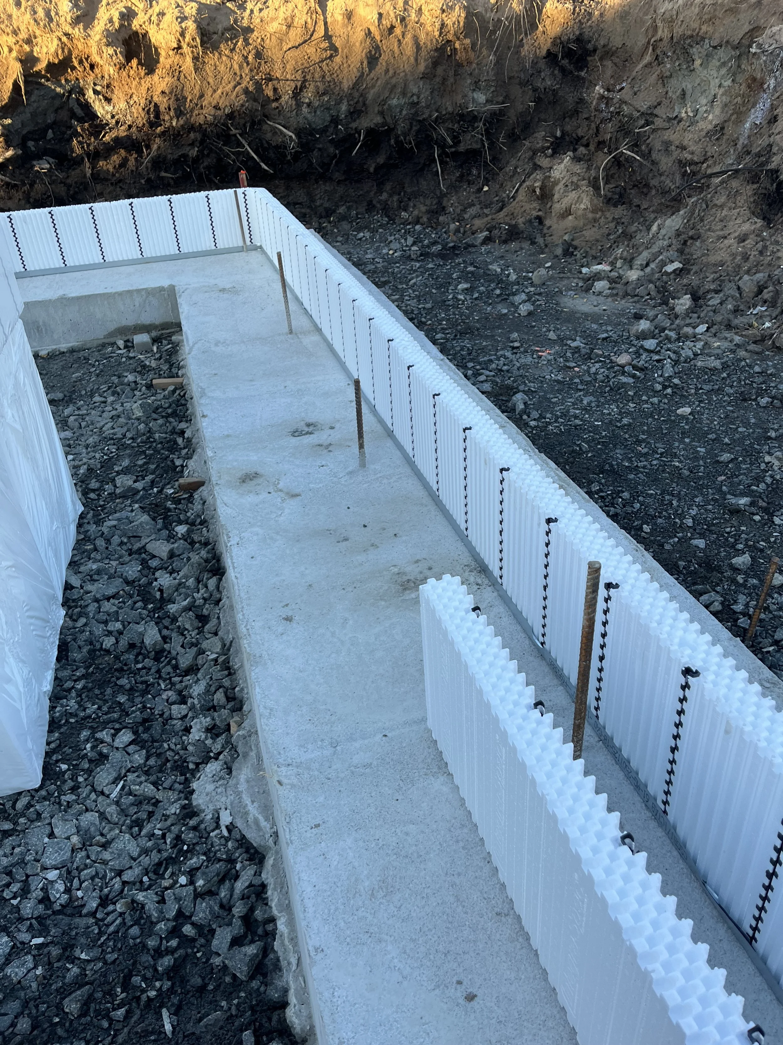 Construction d'une fondation avec un mur en polystyrène, prêt pour la pose du béton, dans un terrain rocheux.