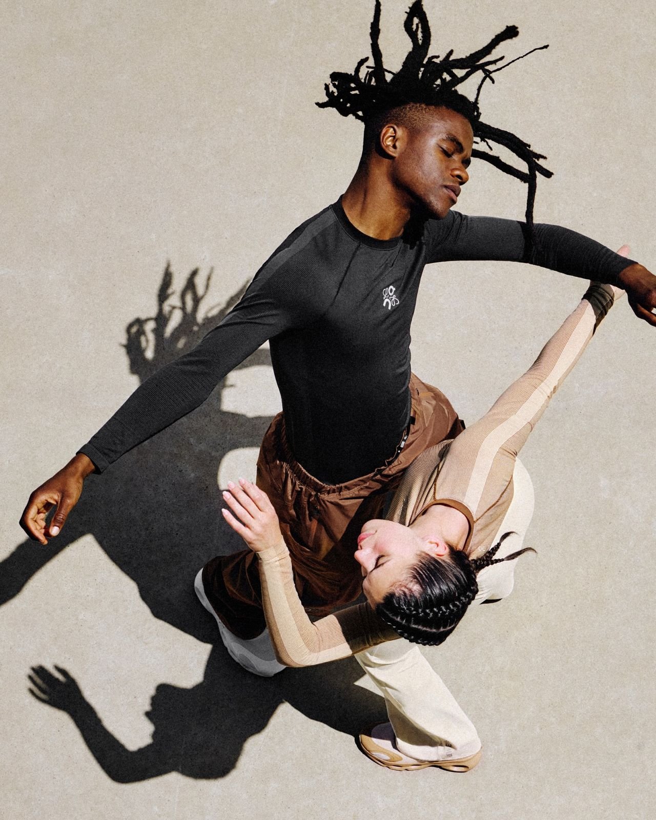 A man and woman performing contemporary dance on a light-colored smooth surface, with shadows cast on the floor.
