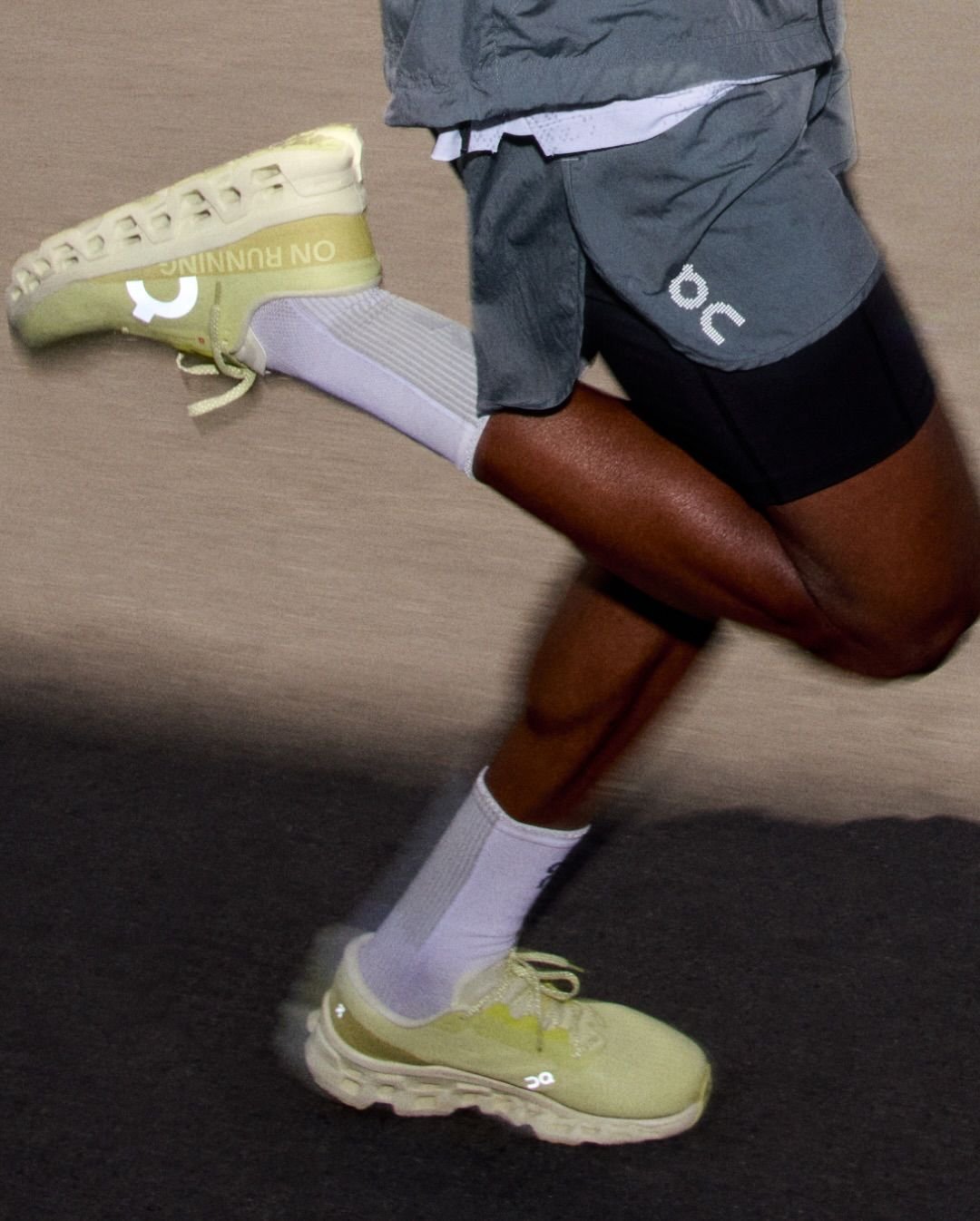 A person is running, wearing yellow running shoes, white socks, black shorts, and a gray jacket.