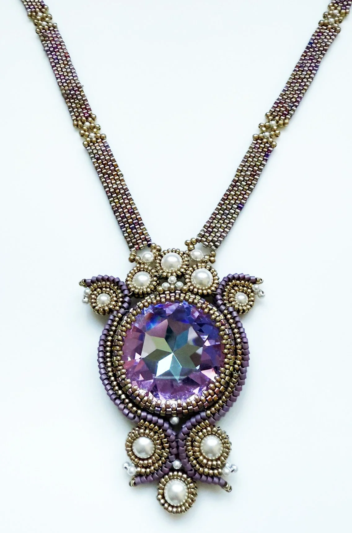 A beaded necklace with a large purple gemstone pendant surrounded by metallic beads, pearls, and intricate beadwork design.