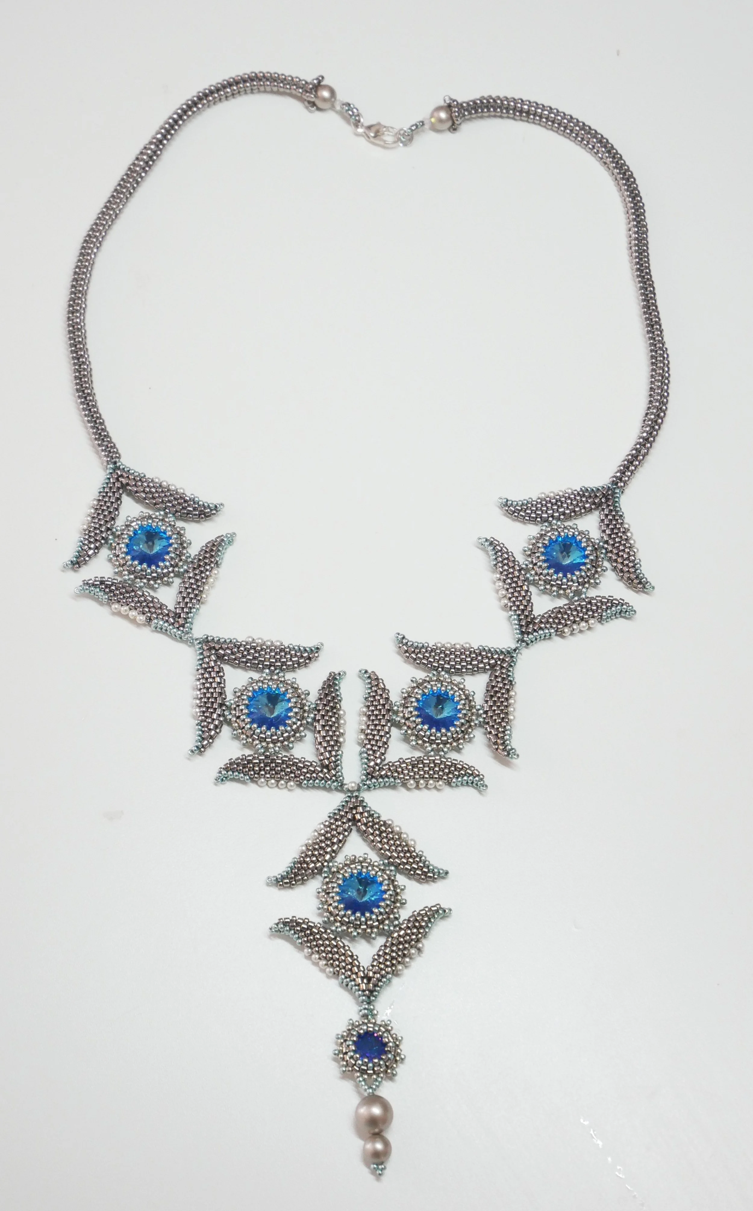 Silver jewelry necklace with blue gemstones, leaf and floral design, and hanging pearls.