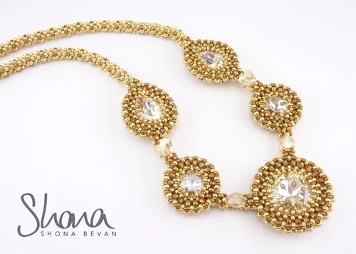 Gold necklace with large clear gemstones and beaded details, featuring five prominent circular gemstone settings, on a white background with a logo that says Shana by Shona Bevan.