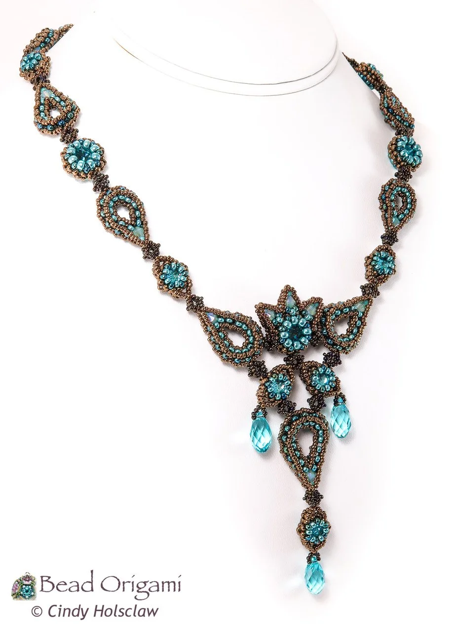 Beaded origami necklace with blue and gold beads displayed on a white bust form.
