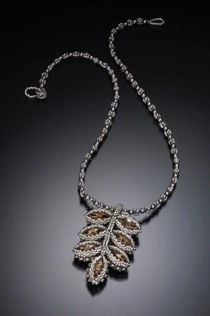 A silver necklace with a large leaf-shaped pendant covered in small rhinestones