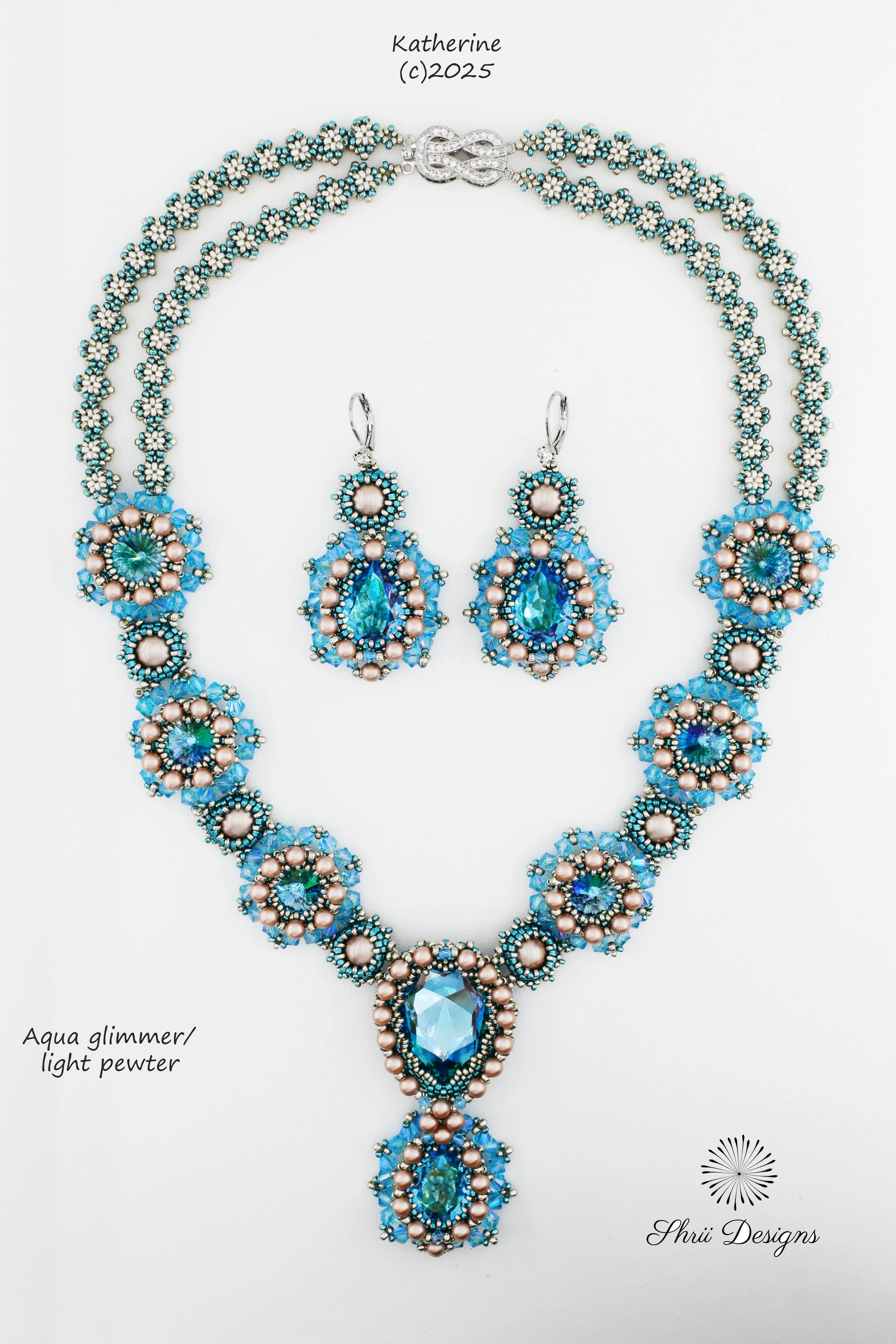 A jewelry set consisting of a necklace and matching earrings. The set features aqua glimmer/light pewter colored beads, blue and pink pearls, and large central aqua-colored crystals. The necklace has a circular clasp and a large pendant. The earrings