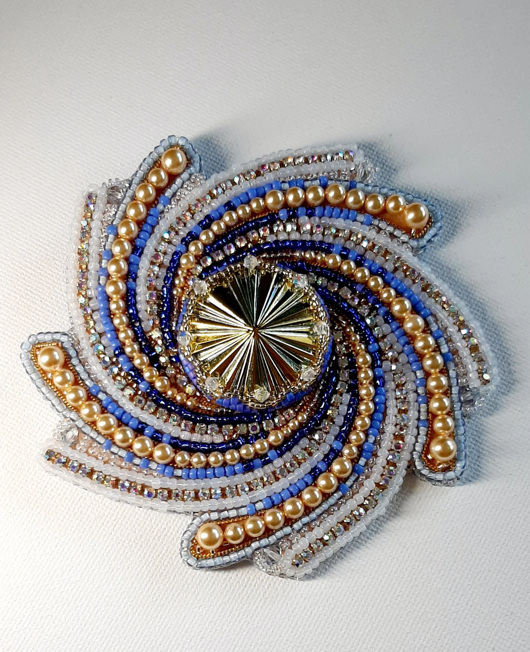 Close-up of colorful beaded brooch with pearls and rhinestones on a white fabric background.