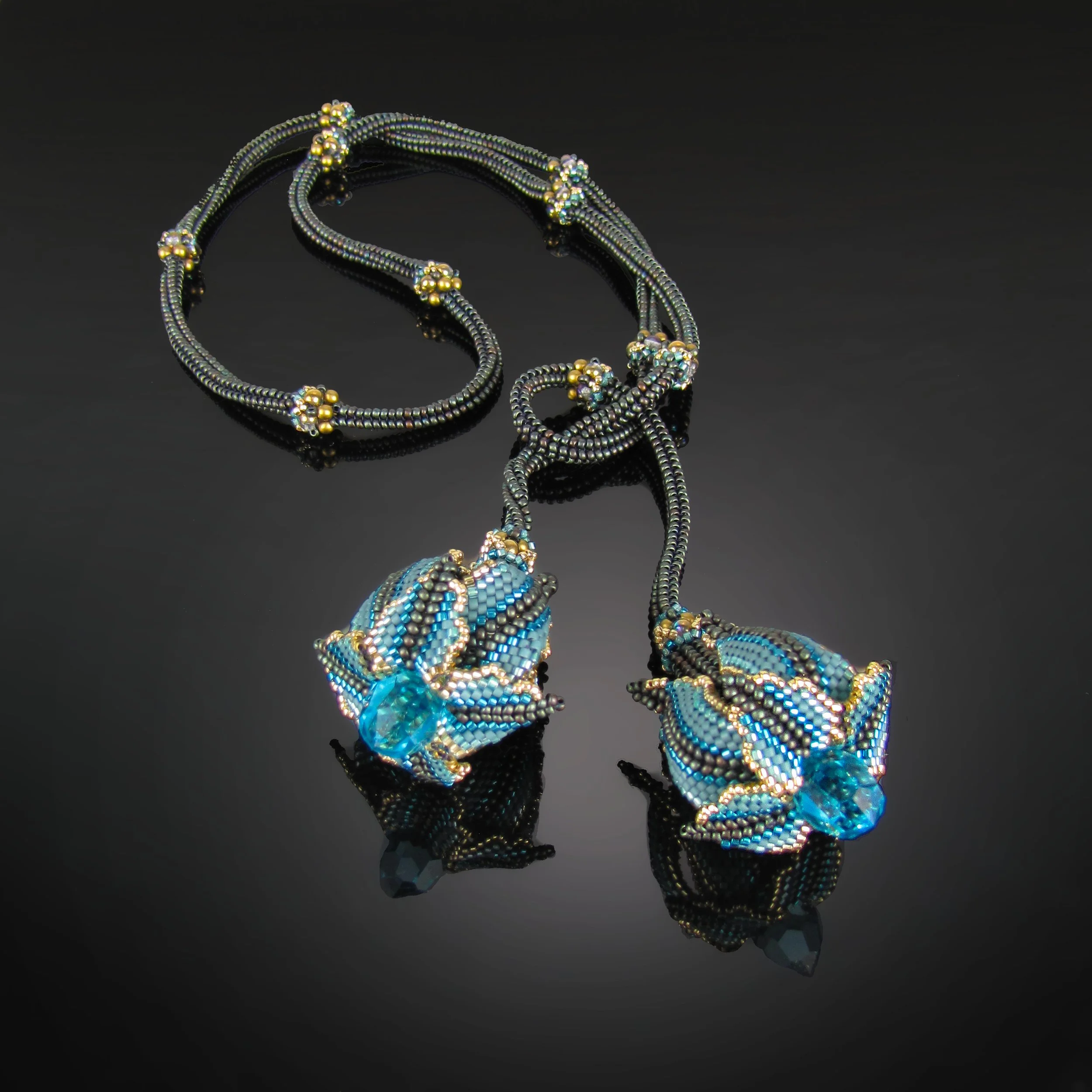 Jewelry set featuring a bracelet and ring with intricate beading, blue and gold accents, set against a black reflective surface.