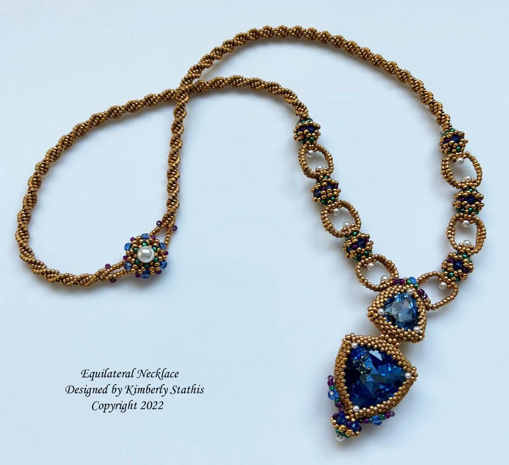 Gold bead necklace with large blue and clear gemstones, and a smaller pearl, designed by Kimberly Stathis.