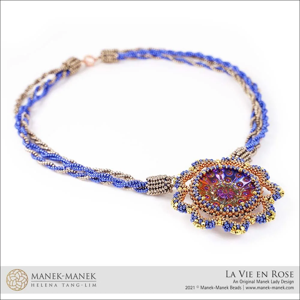 A beaded necklace with a large, ornate, flower-shaped pendant featuring multiple colors, primarily purple, blue, and gold beads, and a central circular element with a reflective surface.