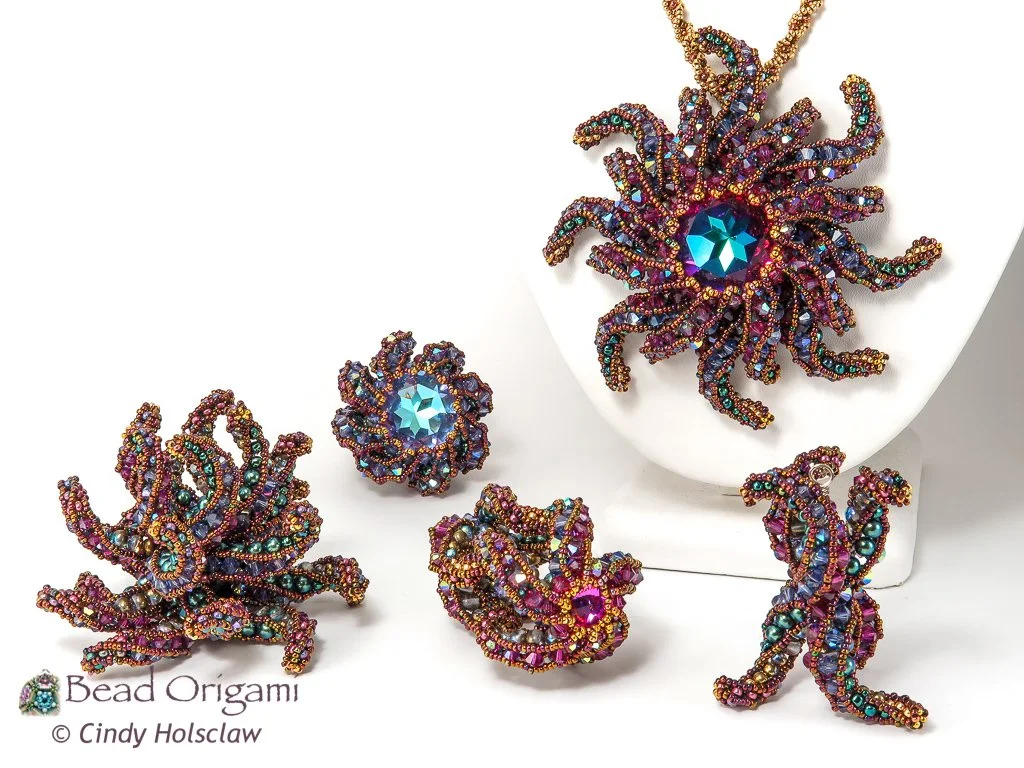 Colorful beaded sculptures resembling sea creatures, including a large octopus, displayed on white surfaces with jewelry components.