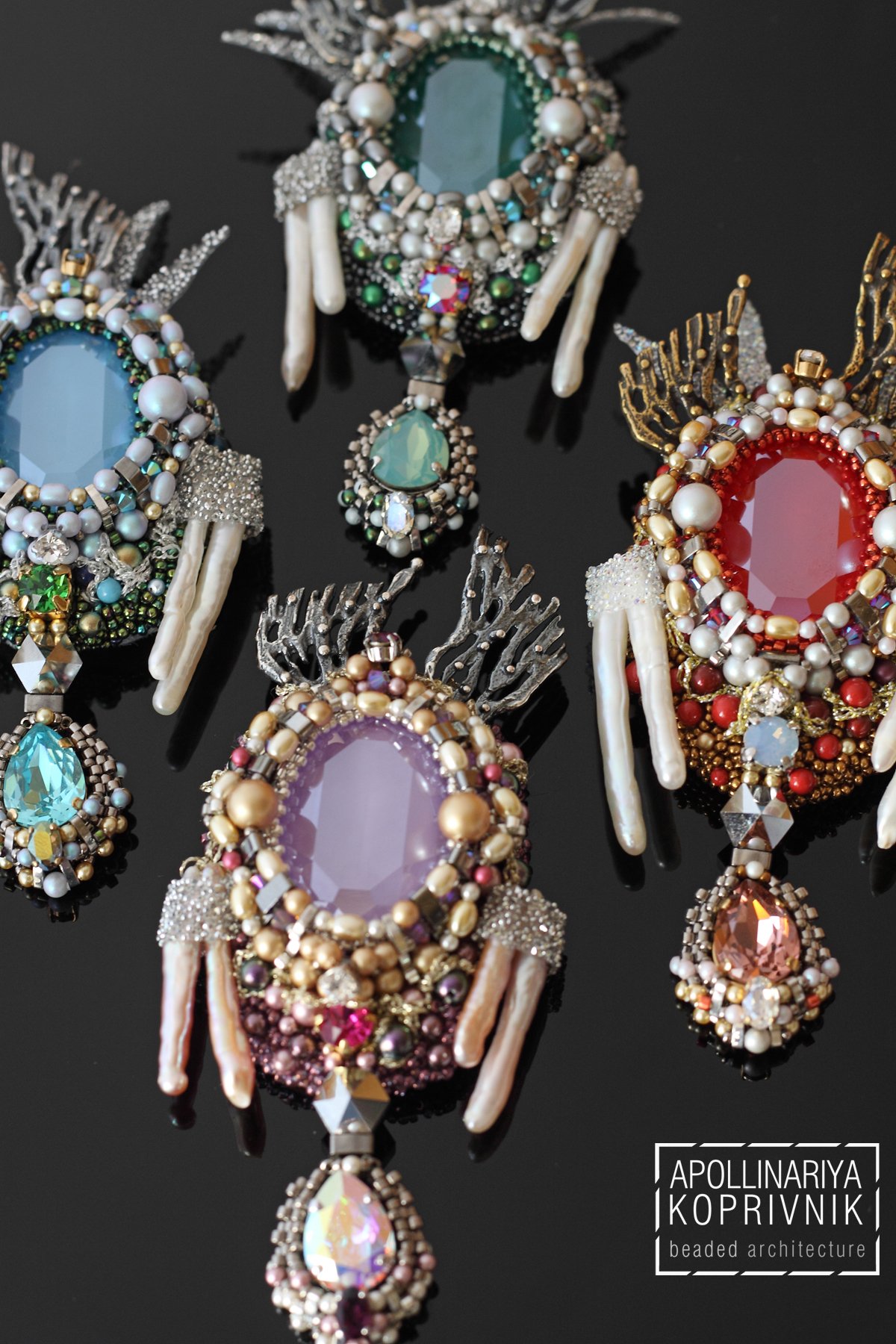 Collection of ornate, decorative brooches or jewelry pieces with large central gemstones, surrounded by pearls, beads, and metallic elements, displayed on a black background.