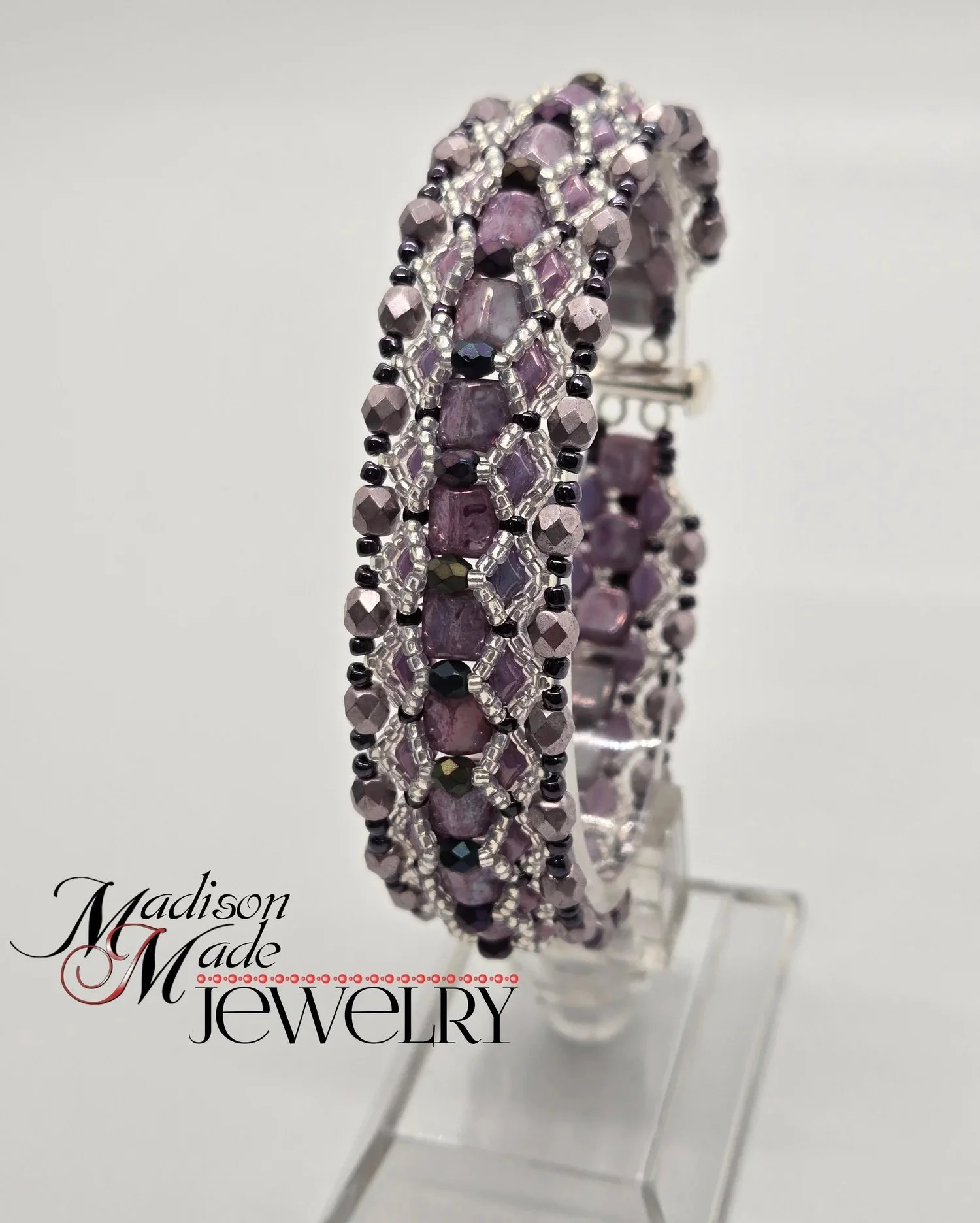 A beaded bracelet with purple, black, and silver beads on a white background. The text 'Madison Made' and 'Jewelry' are visible in the lower left corner.