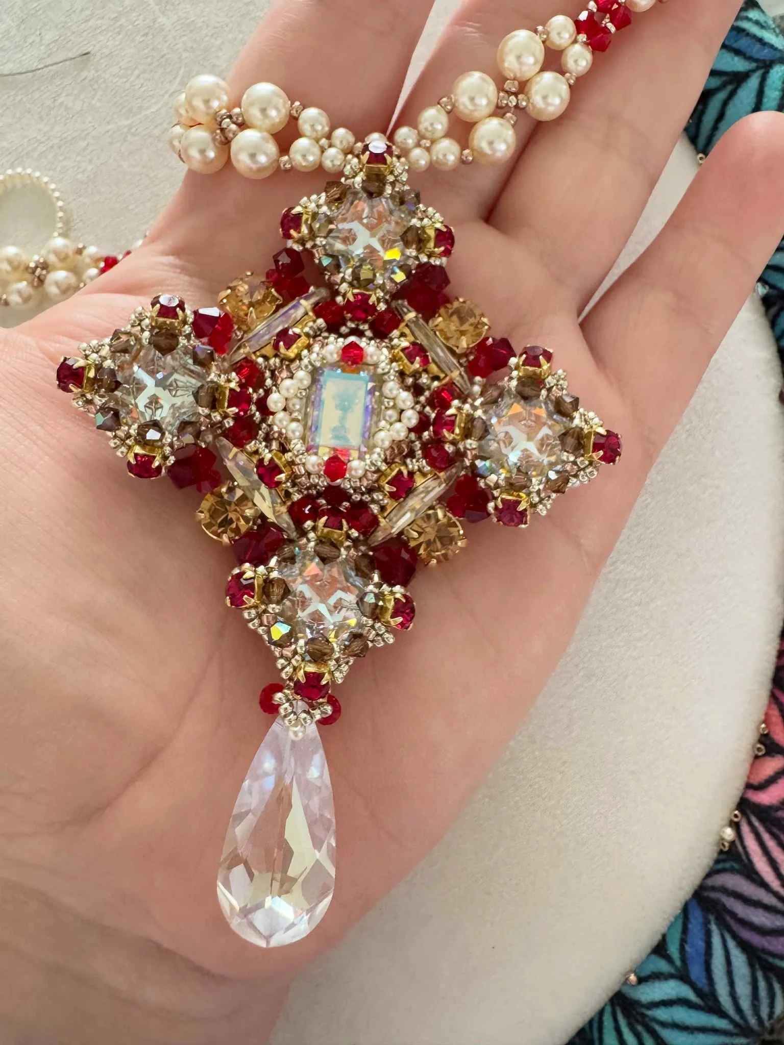 Close-up of a person's hand wearing a large, ornate bracelet made of pearls, red and gold beads, and a large dangling crystal ornament.