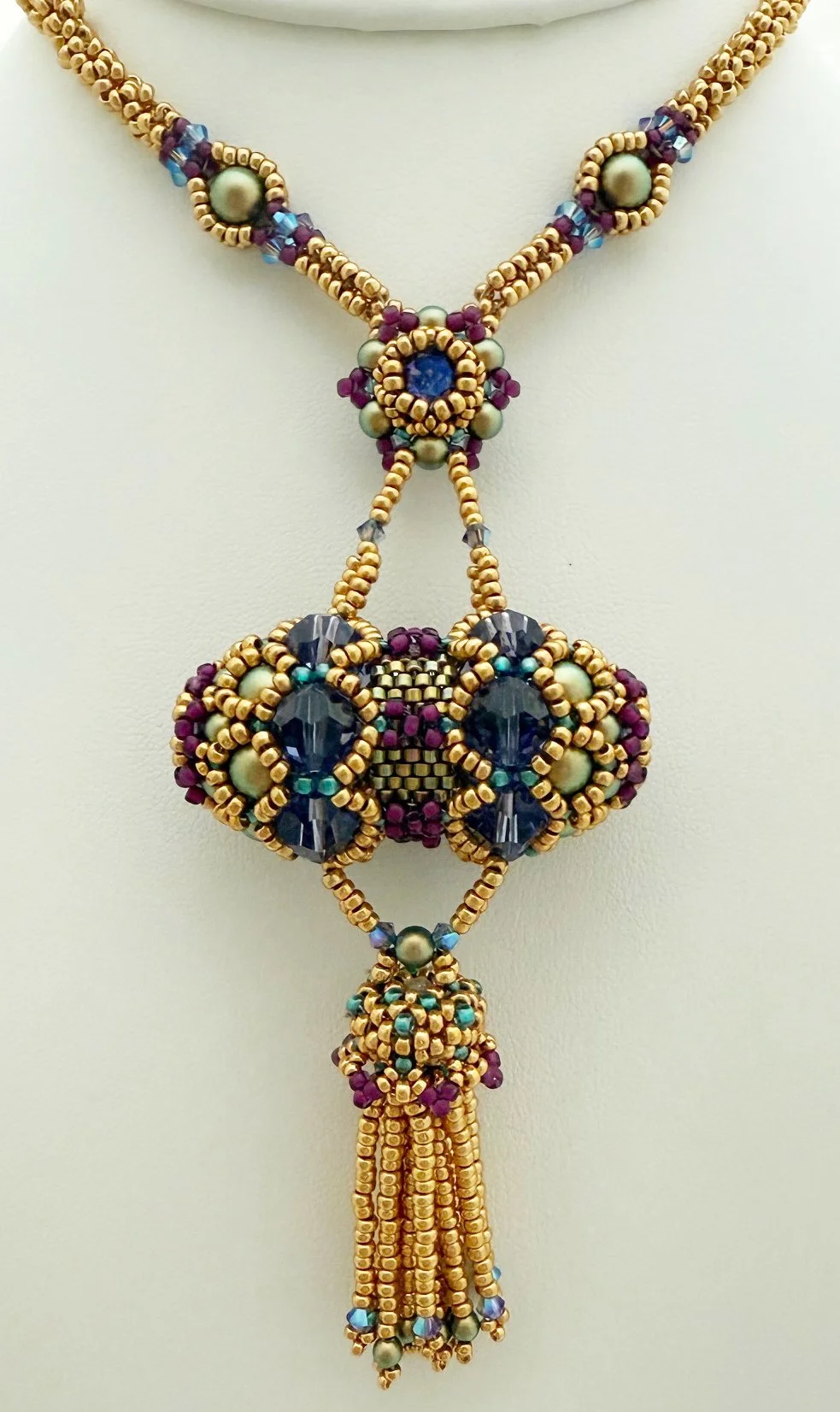A beaded necklace with gold, blue, purple, and pearl-colored beads, featuring intricate designs and a tassel pendant.