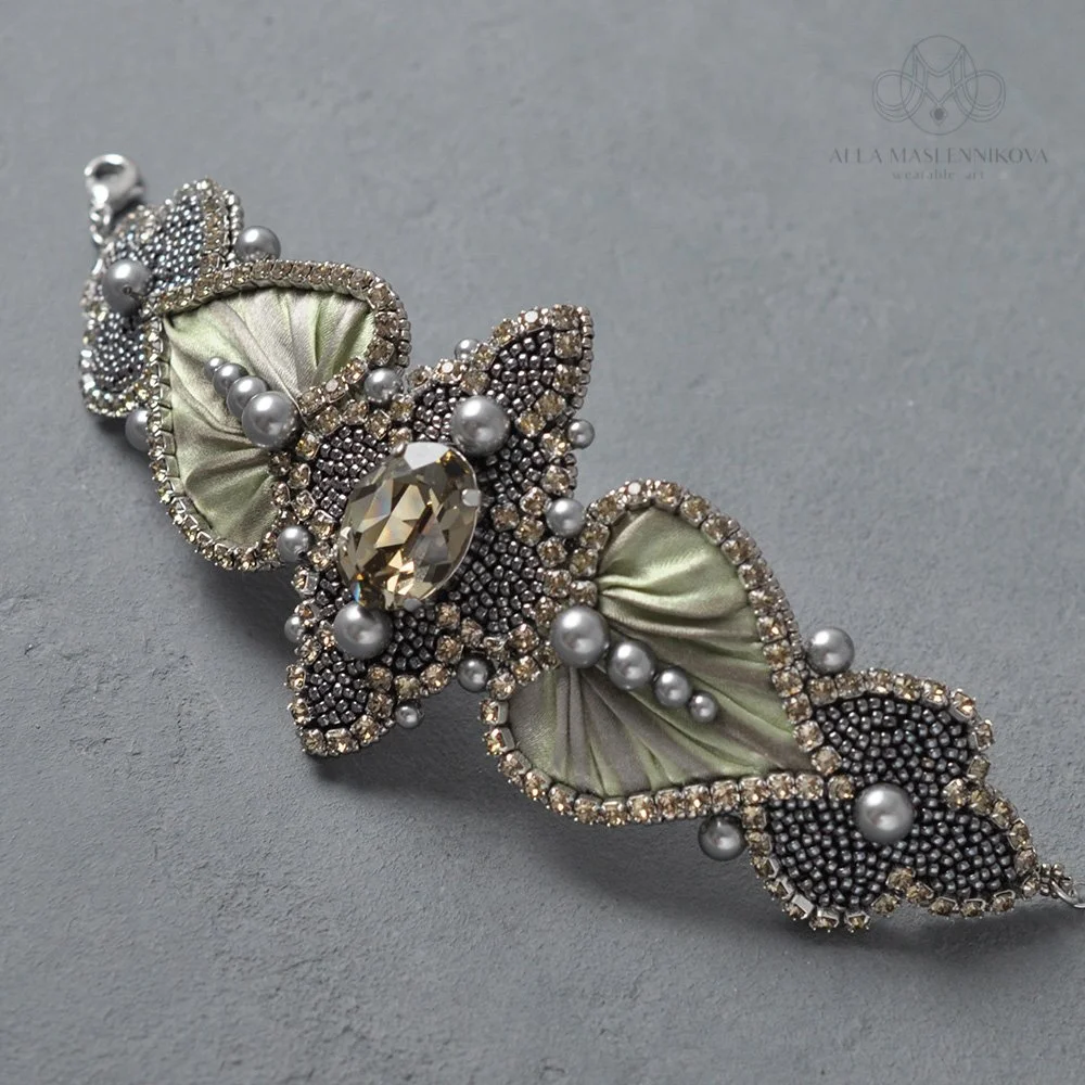 A decorative butterfly-shaped brooch with pearls, small gemstones, and fabric wings on a gray surface.