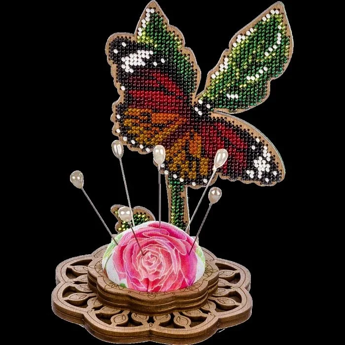 Decorative butterfly with green, red, orange, and white rhinestones perched above a pink rose in a wooden holder with pins