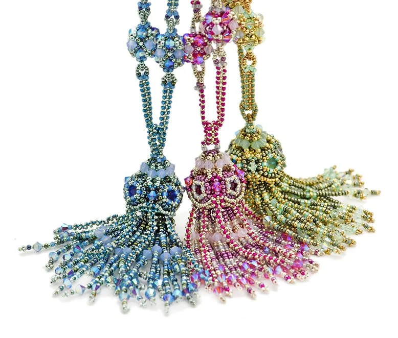 Three beaded necklaces with tassels in blue, pink, and gold colors.